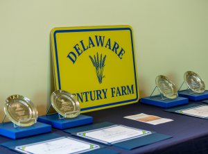 Century Farm Award table with yellow farm lane sign, pewter plaques, certificates, and General Assembly tributes before the ceremony